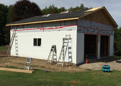 large detached garage build with vinyl siding and shingles being installed