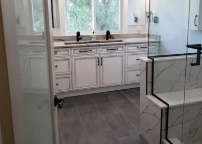 bathroom renovation with large white vanity and a walk-in marble shower with bench and contrasting tile flooring